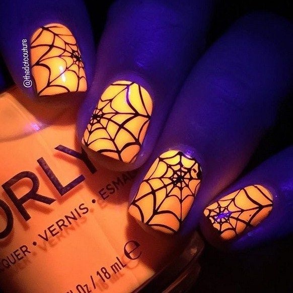 Glow in the dark orange nails with a drawing of spider web, golding the nails polish bottle